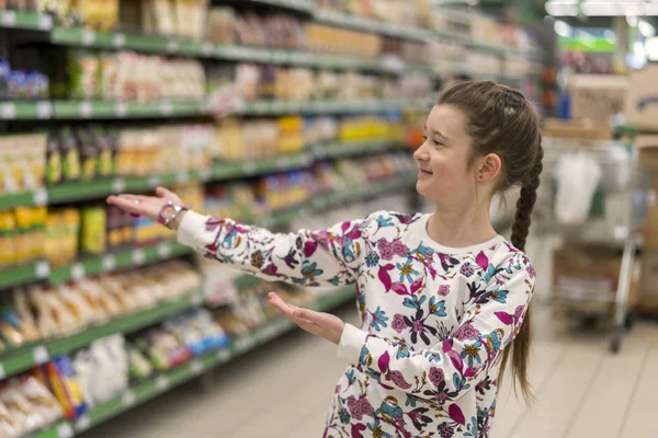 Vidám lány a szupermarketben azt mutatja, a termékek. Egy lány, 8 éves a szupermarketben — Stock Fotó