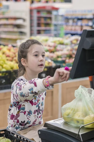 Una chica en un supermercado pesando manzanas. El concepto de niños adultos — Foto de Stock