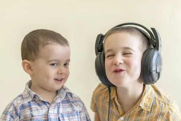 Un niño pequeño con sus auriculares baila con su hermano. Dos hermanitos con camisetas se divierten y bailan . —  Fotos de Stock