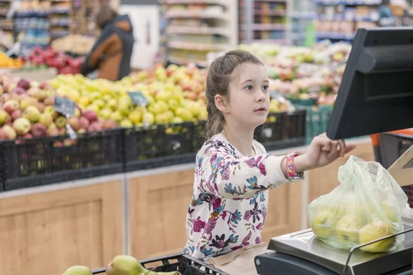 Ένα κορίτσι σε ένα σούπερ μάρκετ που ζυγίζουν τα μήλα. Η έννοια του ενήλικα παιδιά — Φωτογραφία Αρχείου