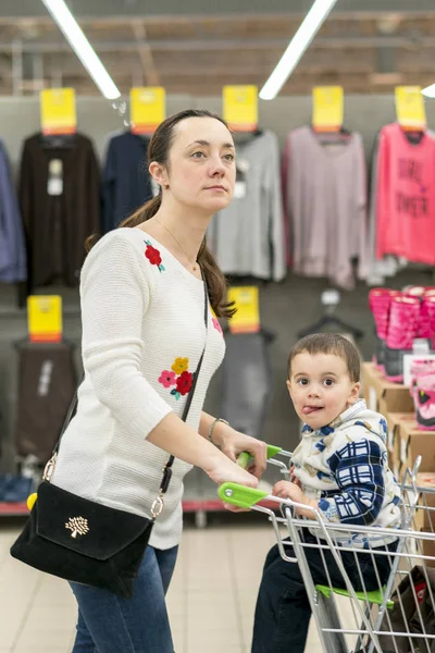 Mãe com uma criança em um carrinho em um centro comercial. Mãe com um filho pequeno num centro comercial. Mãe dirigindo um jovem filho para o centro comercial — Fotografia de Stock