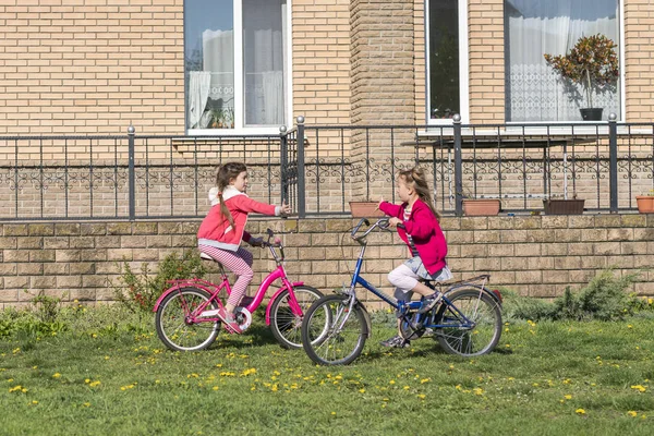 Two girls ride a bicycle. Two sisters ride a bicycle on the lawn in front of the house