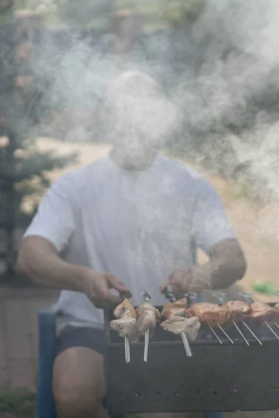 Мужчина с бородой у костра и жареным мясом и сосисками — стоковое фото