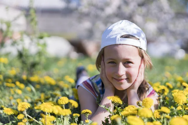 Kleines Mädchen, das auf dem Gras in der Blume liegt. Draußen. Lächelndes Mädchen liegt auf Feld mit Löwenzahn — Stockfoto