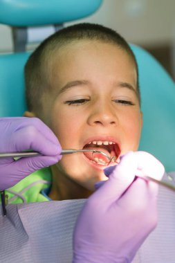 Pediatrik dişçi, dişçi koltuğunda erkek dişlerini muayene ediyor. Diş tedavisi süreci.