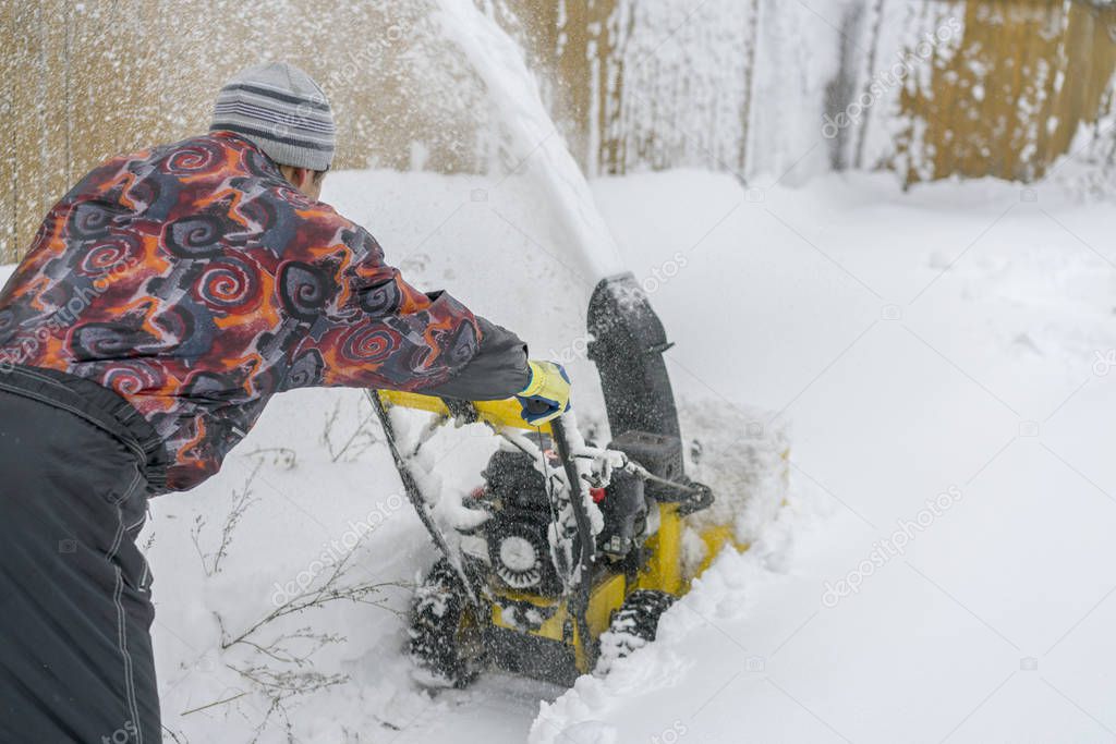 Man operating snow blower to remove snow on driveway. 