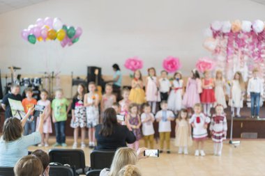 İlkokulda çocuk partisi. Anaokulundaki küçük çocuklar ana-babalarının önünde sahneye çıkıyorlar. Anaokulunda tatil. Bulanık.