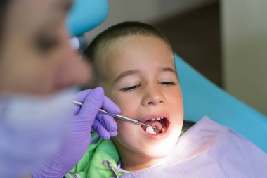 Pediatrik diş hekimi, dişçi koltuğunda küçük çocukların dişlerini muayene ediyor..