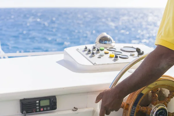 Captain standing at steering wheel of motor boat in the blue ocean during the fishery day.