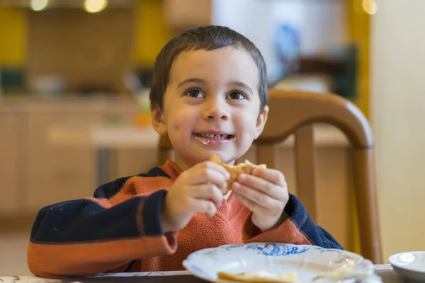 Happy little boy eating pancakes. Portrait of small cute little boy child sitting by the table at home eating pancakes.