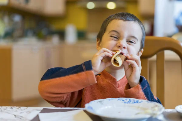 Happy little boy eating pancakes. Portrait of small cute little boy child sitting by the table at home eating pancakes.