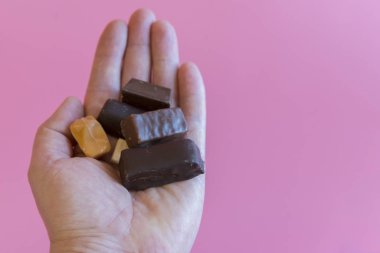 Pembe arka planda çikolatalı bir el. Tatlıların tadını çıkarıyorum. Güzel bağımlılık konsepti. Tatlı için aşk kavramı. Boşluğu kopyala.