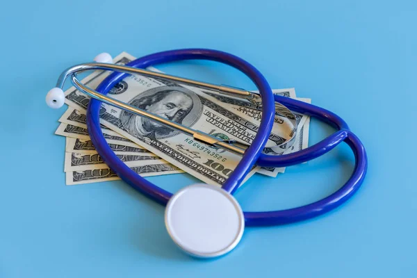 Stethoscope and dollar bills on blue background. Mock-up with copy space for your text. Concept of health care costs and medical expenses, saving money for health insurance.