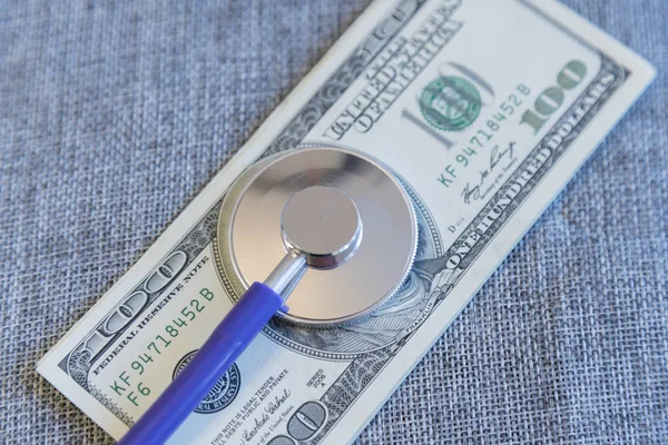 Financial checkup - Stethoscope on pile of U.S. hundred dollar bills on grey background.