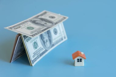 Depicts saving for house or flat manageable. Mortgage concept. House figurine and house made of dollars on blue background.