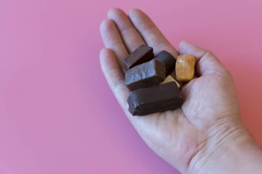 Hand with chocolates on pink background. Enjoying sweets. Sweet addiction concept. The concept of love for sweets. 