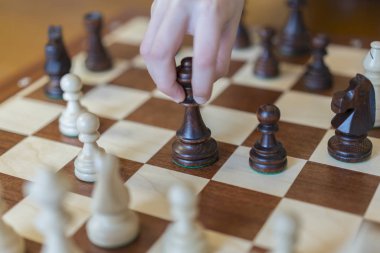 Businessman hand holding chess piece on board with white background, playing wooden chess pieces.