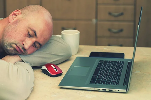 man sleeping on the table with laptop at home. bald man sleeping at his working place home office. Portrait of a man lying down at the desk near the laptop, education, business concept photo. Lifestyle. toned. close up.