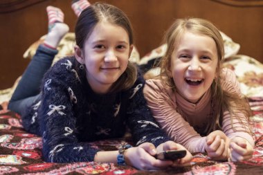 Televizyon ya da film izleyen iki mutlu kız. Yatakta yatan ve en sevdikleri dizileri izleyen iki güzel kız kardeşin yatay fotoğrafı..