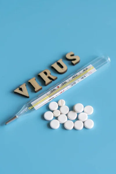 thermometer, pills and the inscription virus on a blue background. Virus treatment concept. vertical photo.