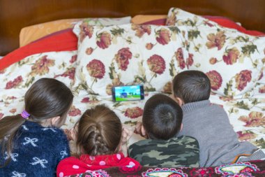 Yatakta dört çocuk ebeveyn yatağında akıllı telefondan çizgi film izliyor.. 