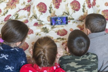 Yatakta dört çocuk ebeveyn yatağında akıllı telefondan çizgi film izliyor.. 