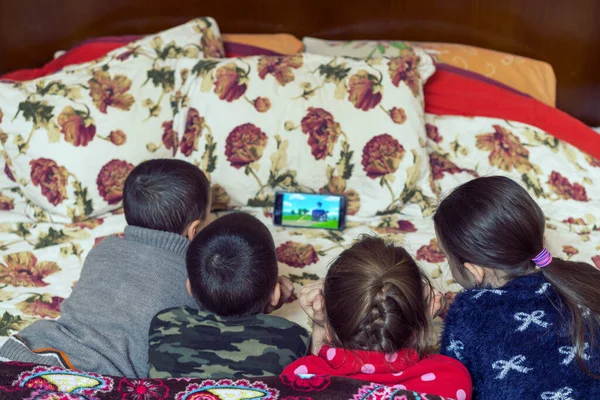 Four children in bed watching cartoon on smartphone on the parents bed.
