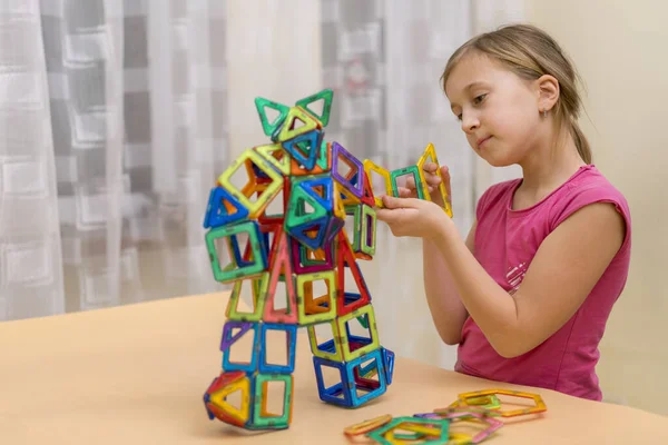 Little girl playing colorful magnet plastic blocks kit at indoor playground. Early childhood development.