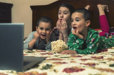 Çocuklar yatmadan önce dizüstü bilgisayara bakıp çizgi film izliyorlar. Yatakta dizüstü bilgisayarda film izleyen üç çocuk..