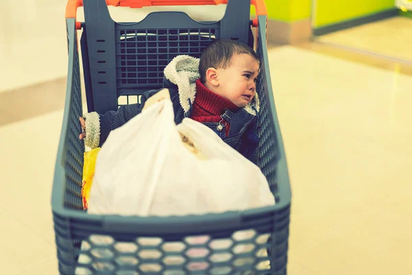 Malý chlapec pláče v supermarketu ve vozíku. Zapomenuté dítě. tónovaný — Stock fotografie