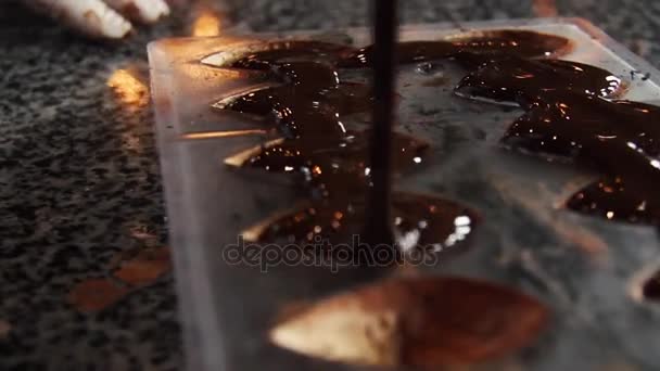 Fábrica de chocolate. El confitero en guantes estériles vierte chocolate caliente en el molde. Chocolates hechos a mano. El chocolate templado se vierte en el molde. Producción de chocolates . — Vídeo de stock