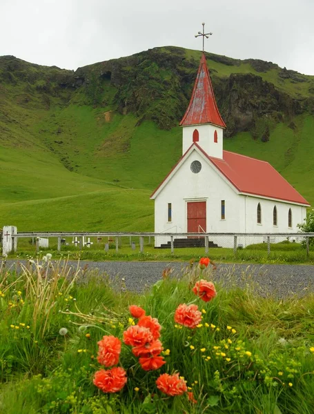 Summer walk in the vicinity of the town of Vic, red flowers and a church by the road to the black beach of Reinisfjara