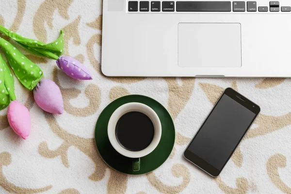 Beautiful flowers and coffee on sofa with cell phone and computer