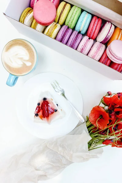 Morning poppy flowers bouquet and french macarons with tasty cake and cappuccino on white table