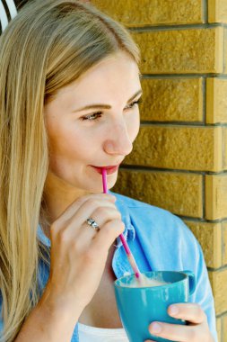 Genç güzel sarışın kız kahve içme ve hakkında bir şey düşünüyorum. Çekici kız fincan kapuçino holding