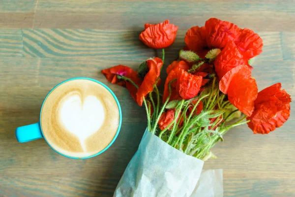 Cup of aroma cappuccino and bouquet fo poppy flowers on wooden table background
