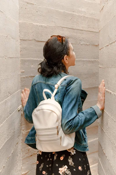 Attractive young woman stands between concrete walls. Caucasian girl in casual jeans looks up.