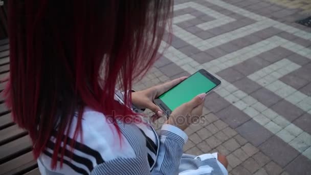 Chica en vestido sentado en el parque y el uso de teléfono inteligente pantalla clave de croma — Vídeo de stock