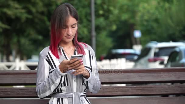 Mooi meisje met smartphone in stadspark, pinc haren — Stockvideo