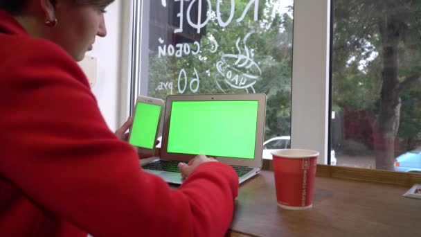 Chica de negocios en un coffeshop, trabajando con el ordenador portátil y el teléfono al mismo tiempo — Vídeos de Stock