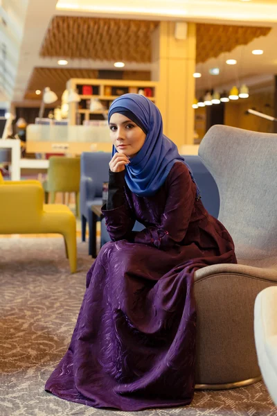 Красивая мусульманка в современной восточной одежде сидит в кресле в вестибюле — стоковое фото