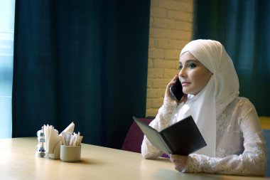 kafede oturan ve telefonda konuşurken bir beyaz gelinlik güzel Müslüman kadın