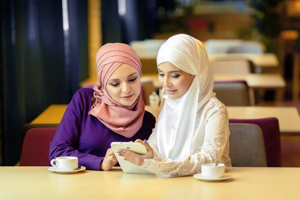 Två muslimska kvinnor i ett café, shop online med elektroniska tablett — Stockfoto