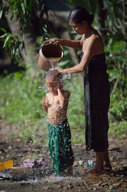 Anne çocuğunu dışında bir kova ile bir köy sokak su dökerek yıkama