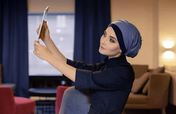 Очаровательная восточная девушка в мусульманской одежде делает селфи на электронном гаджете — стоковое фото