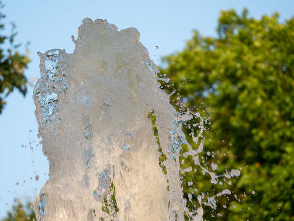 Фонтан воды на фоне голубого неба с деревьями на заднем плане, выбранный фокус
