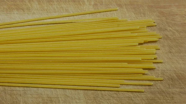 Zbliżenie niegotowanego spaghetti na zadrapanym drewnianym desce, widok z góry — Zdjęcie stockowe
