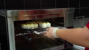 Şeffaf steril eldivenli Asyalı kız aşçı gümüş ocağa yakın kızartma için folyolu özel tabakta bir sürü lezzetli rulo koyar. Suşi ustası yemek ve satış için rulo yapıyor..