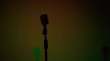 Profesyonel konser klasik mikrofon kaydı için ya da karanlık boş retro kulübünde seyircilerle konuşmak için. Sahne ışıkları çok renkli arkaplanda krom mikrofon siluetinde parlıyor.