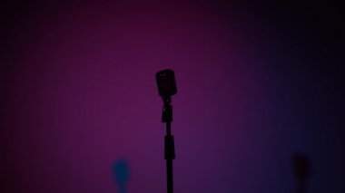 Concert vintage glare microphone for record or speak to audience on stage in dark empty retro club. The lights of spotlights are getting brighter and shine on a chrome mic on pink blue background.
